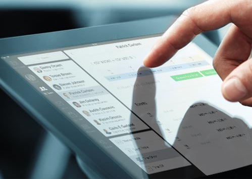 A hand is shown interacting with a tablet screen, which displays a scheduling or calendar application with a list of names, dates, and times. The finger is tapping on an item, indicating an action or selection.